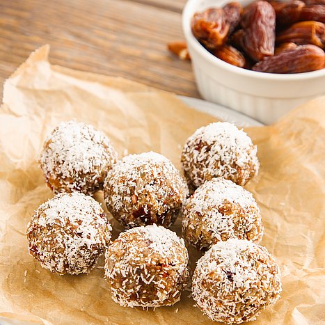 Energy-Balls auf einem Teller, daneben Schlüsseln mit Mandeln und Datteln.
