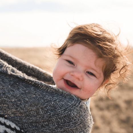 Baby in einem Tragetuch lacht in die Kamera.