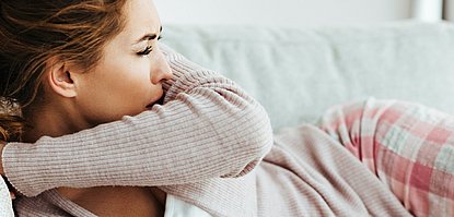 Frau auf der Couch hustet.